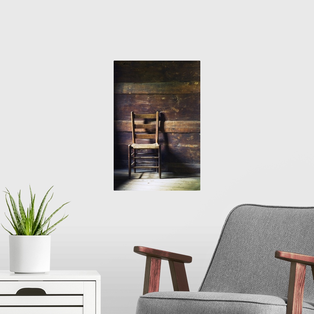 A modern room featuring Portrait photo of an empty ladderback wooden chair sitting in a beat up wood slat wall room with ...