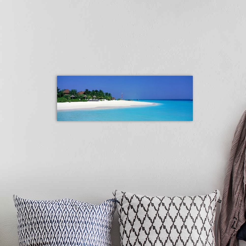 A bohemian room featuring This panoramic photograph is of a beach in Maldives with huts pushed back and surrounded by trees...