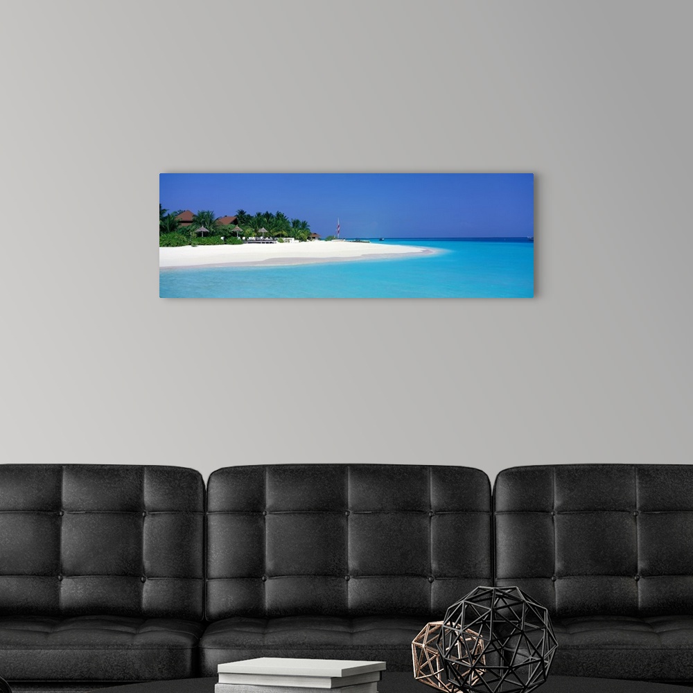 A modern room featuring This panoramic photograph is of a beach in Maldives with huts pushed back and surrounded by trees...