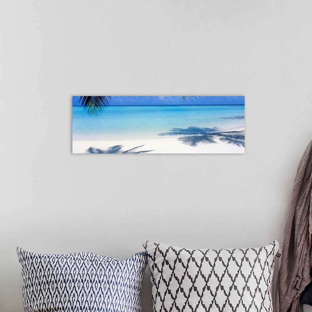 A bohemian room featuring Panoramic landscape photograph of a tropical beach with palm trees casting shadows in the sand.