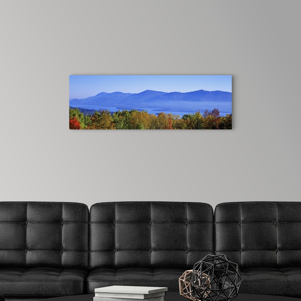 A modern room featuring Panoramic photograph on a large wall hanging of the tops of autumn trees in front of Lake George,...