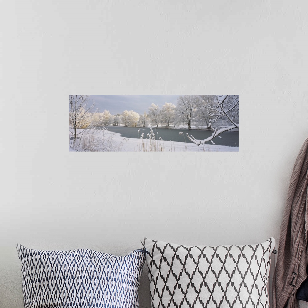 A bohemian room featuring A frozen lake is photographed and surrounded by snow covered trees and land.