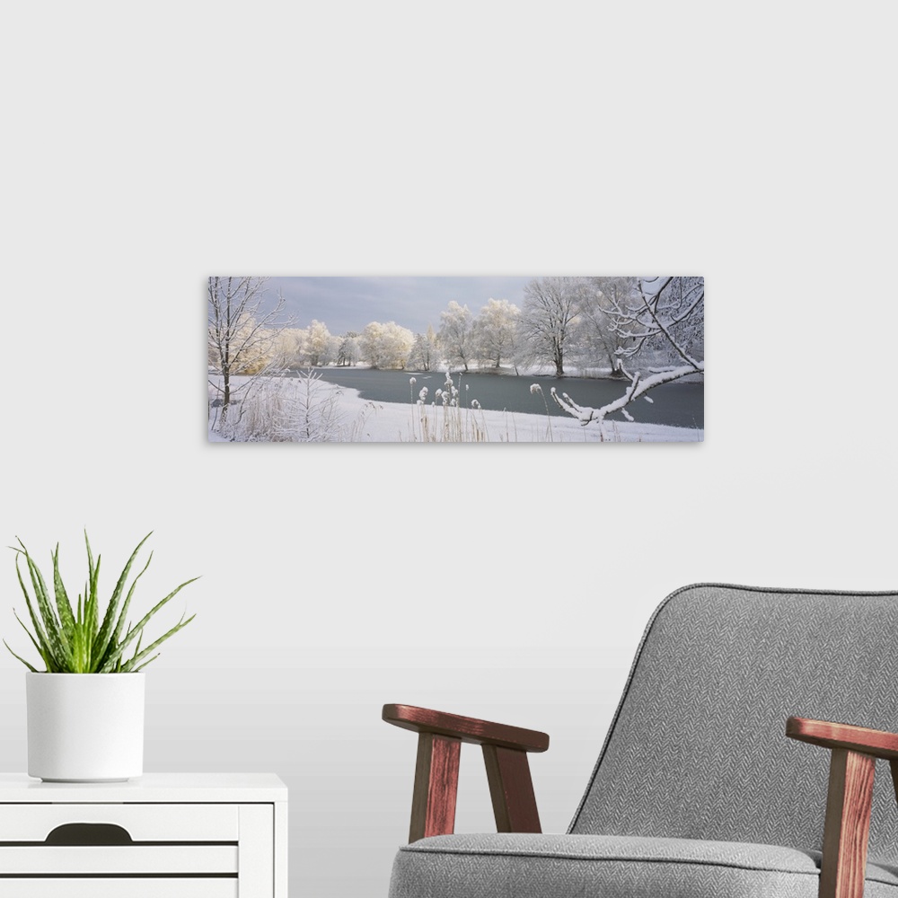 A modern room featuring A frozen lake is photographed and surrounded by snow covered trees and land.