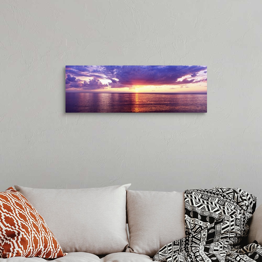 A bohemian room featuring Sun setting over the Great Lake, bordered by puffy clouds and the calm waters, casting its glowin...