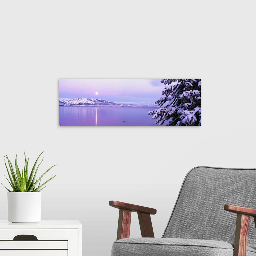 A modern room featuring Wide angle photograph of the sun setting over Lake Tahoe, snow covered mountains in the backgroun...