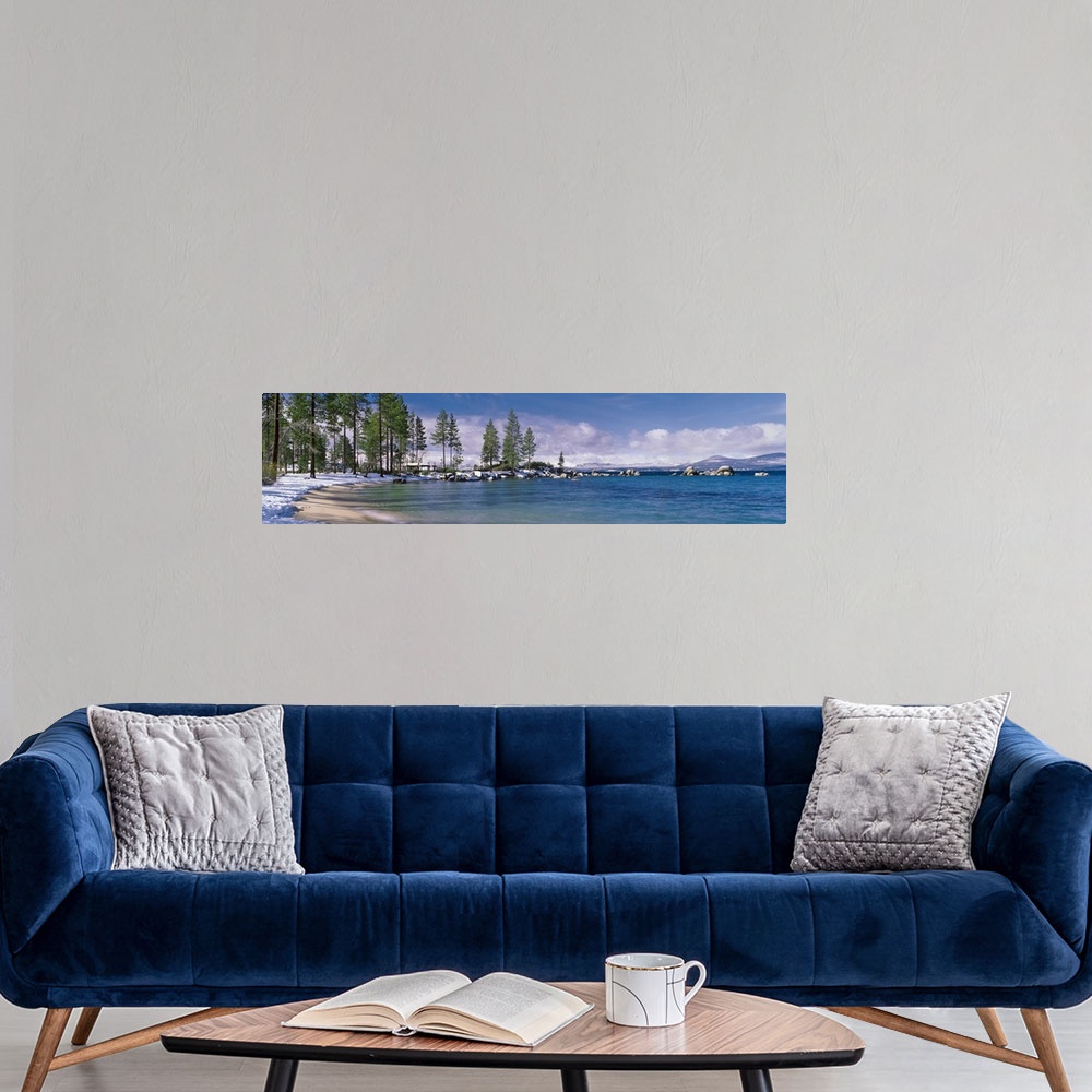A modern room featuring This large panoramic piece is a photograph of the Lake Tahoe coast. Pine trees line the snow cove...