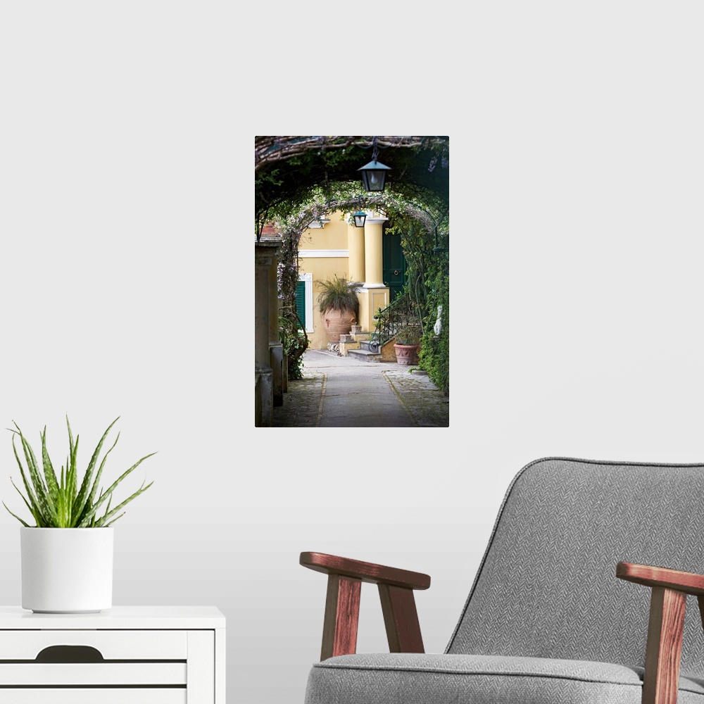A modern room featuring A vertical photograph or a walkway under vine covered arches in a scenic Italian city.