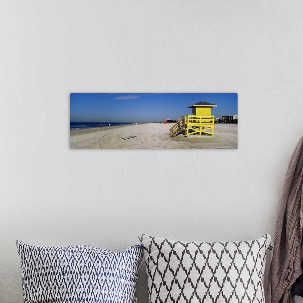 A bohemian room featuring A panoramic photograph of a mostly empty beach, there is a small shelter and abandoned surfboard ...
