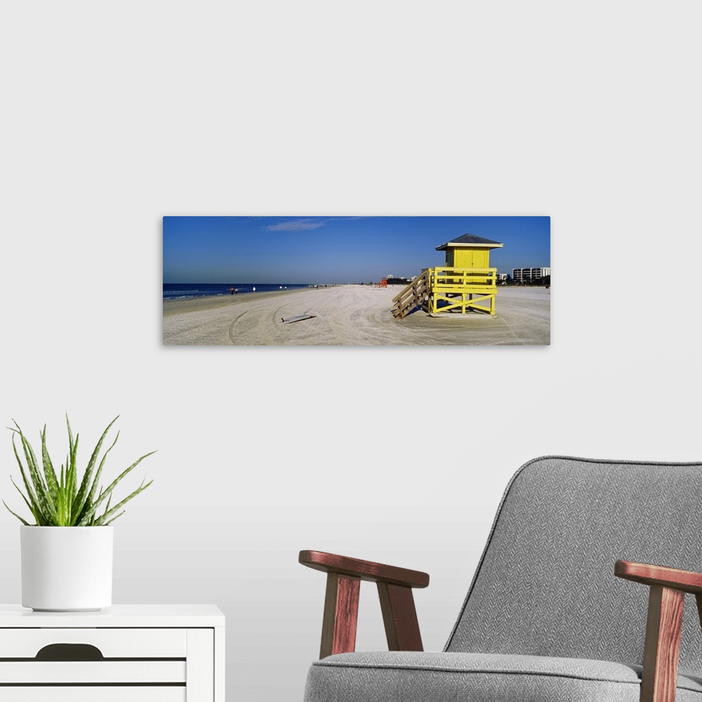A modern room featuring A panoramic photograph of a mostly empty beach, there is a small shelter and abandoned surfboard ...