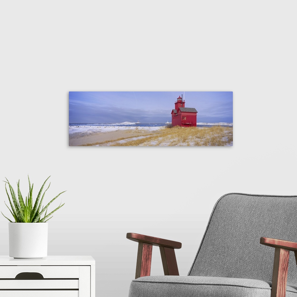 A modern room featuring Lonely red light house on the edge of the water on a snowy beach, standing out against the pale c...