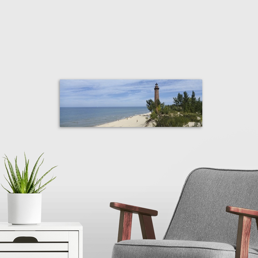 A modern room featuring A light house on a sandy shore obscured by costal plant life and a partially cloudy sky.