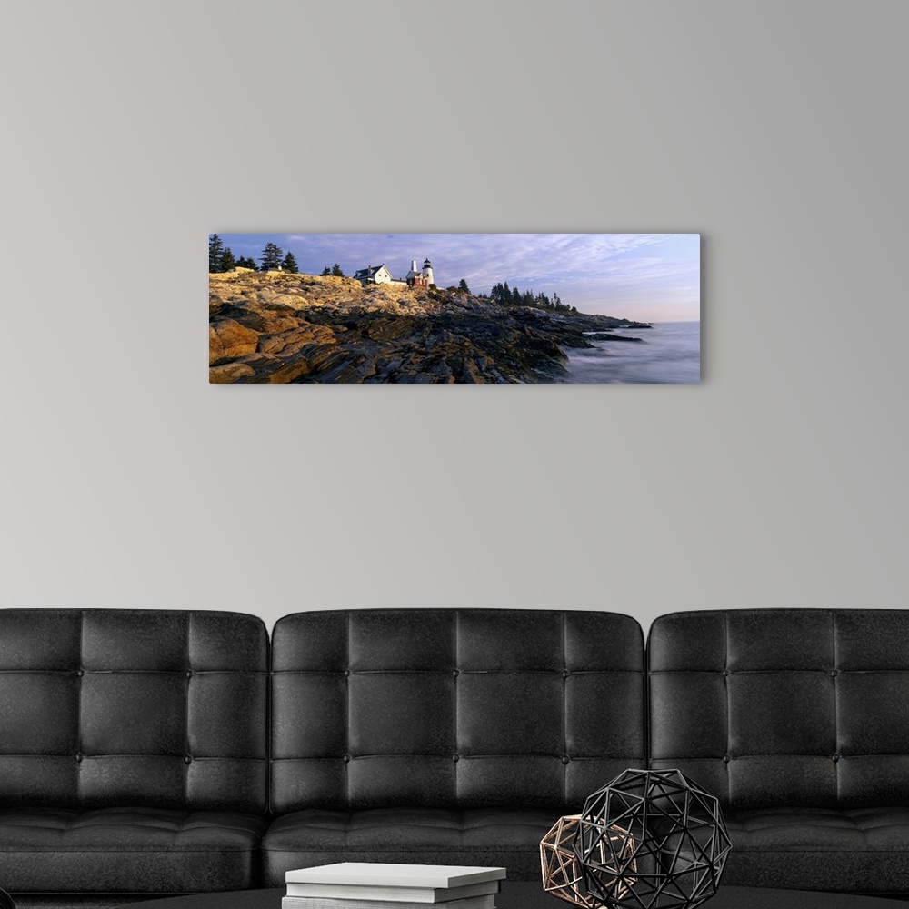 A modern room featuring A large panoramic photograph taken from sea level and looking up at a lighthouse. Rocks take up m...