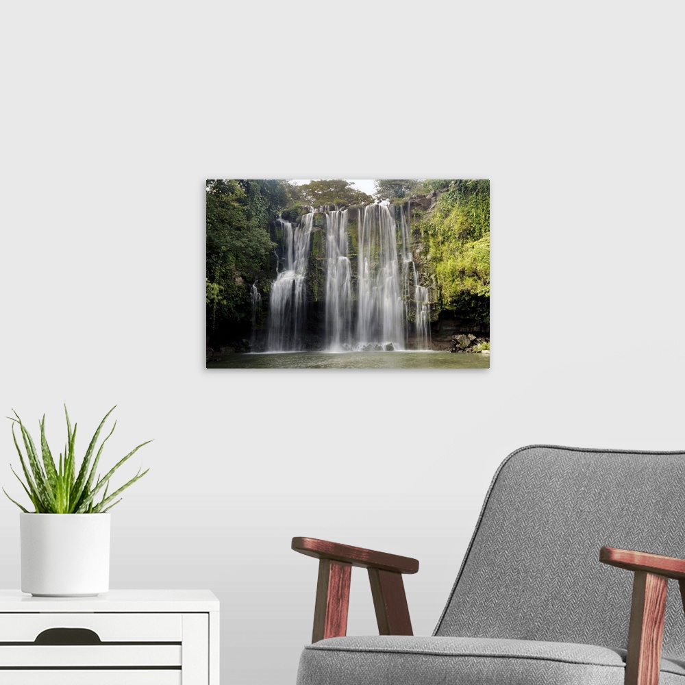 A modern room featuring Long exposure photograph of a waterfall over a rocky cliff in Central America with leafy jungle v...