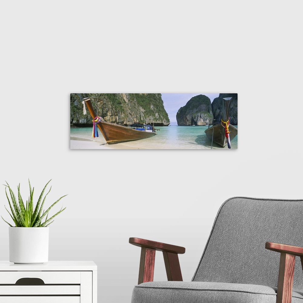A modern room featuring Panoramic photograph of two big canoes docked in sand at the shoreline with huge rock formations ...