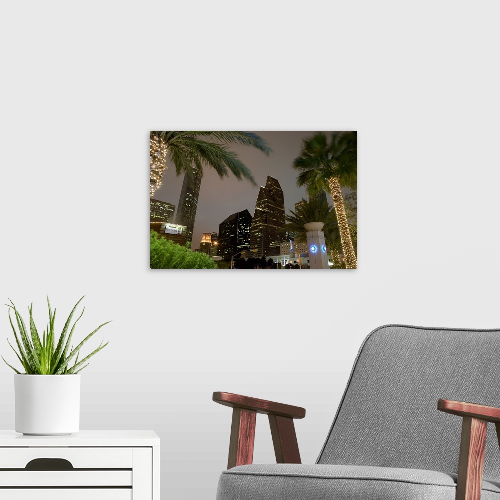 A modern room featuring Landscape, large photograph, looking up through several palm trees at the lit skyscrapers of the ...