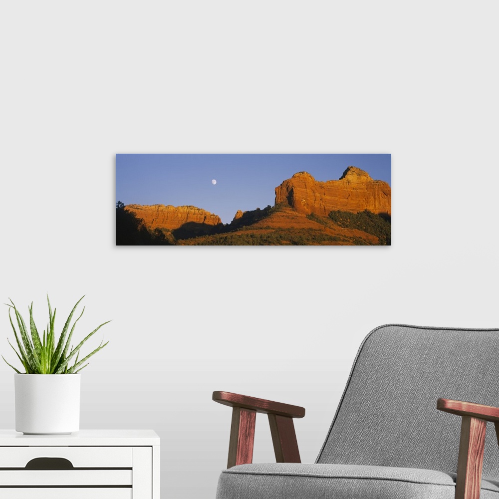 A modern room featuring A panoramic photograph of the setting sun illuminating rock cliffs as the moon rises between them.