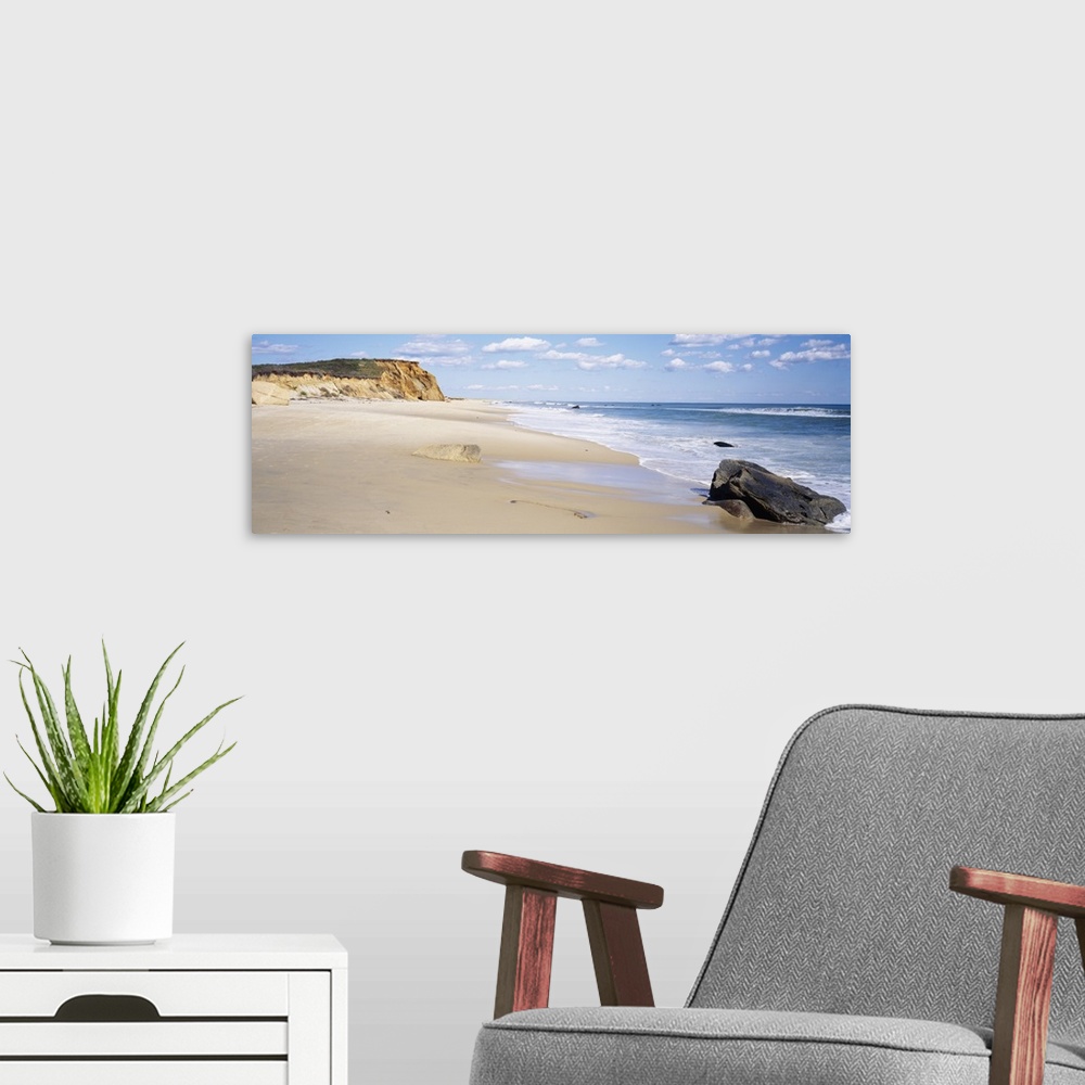 A modern room featuring Panoramic photograph of shoreline with surf, large rock, and cliff in the distance under a cloudy...