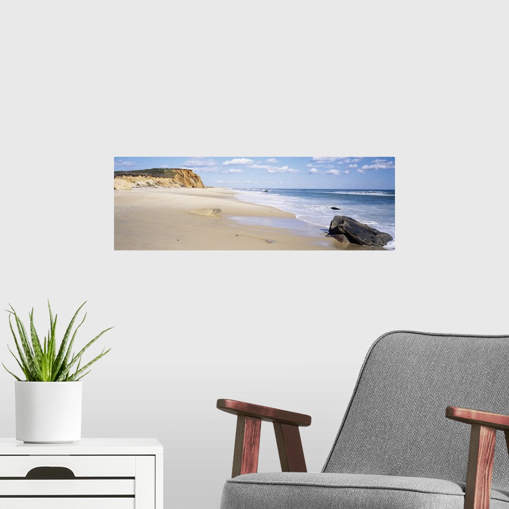 A modern room featuring Panoramic photograph of shoreline with surf, large rock, and cliff in the distance under a cloudy...