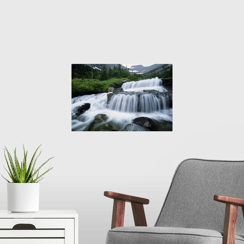A modern room featuring Big print of water rushing down small waterfall areas of rocks in a river surrounded by rugged mo...