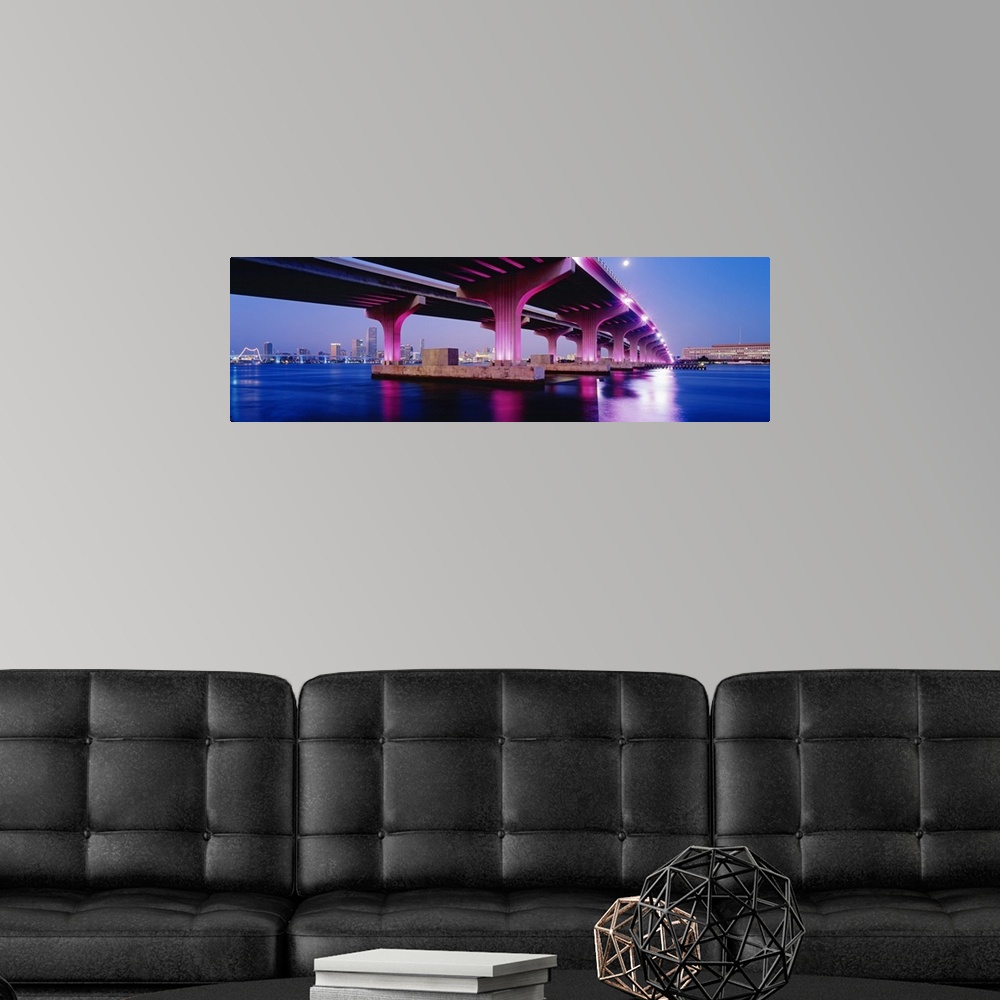 A modern room featuring Panoramic photograph on a big canvas of the MacArthur Causeway, lit up at night and reflecting in...