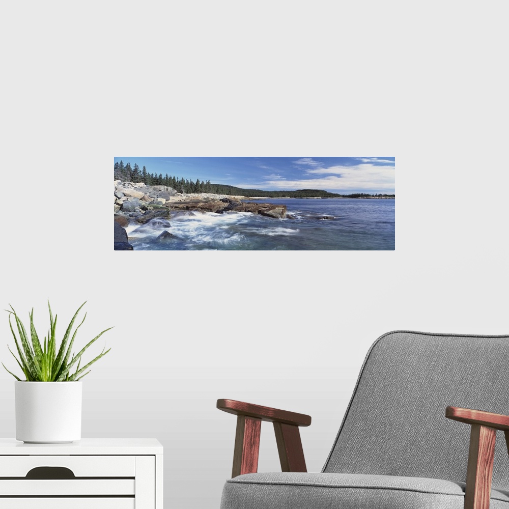A modern room featuring Panoramic photograph of rocky shoreline with surf.  There are trees in the distance under a cloud...