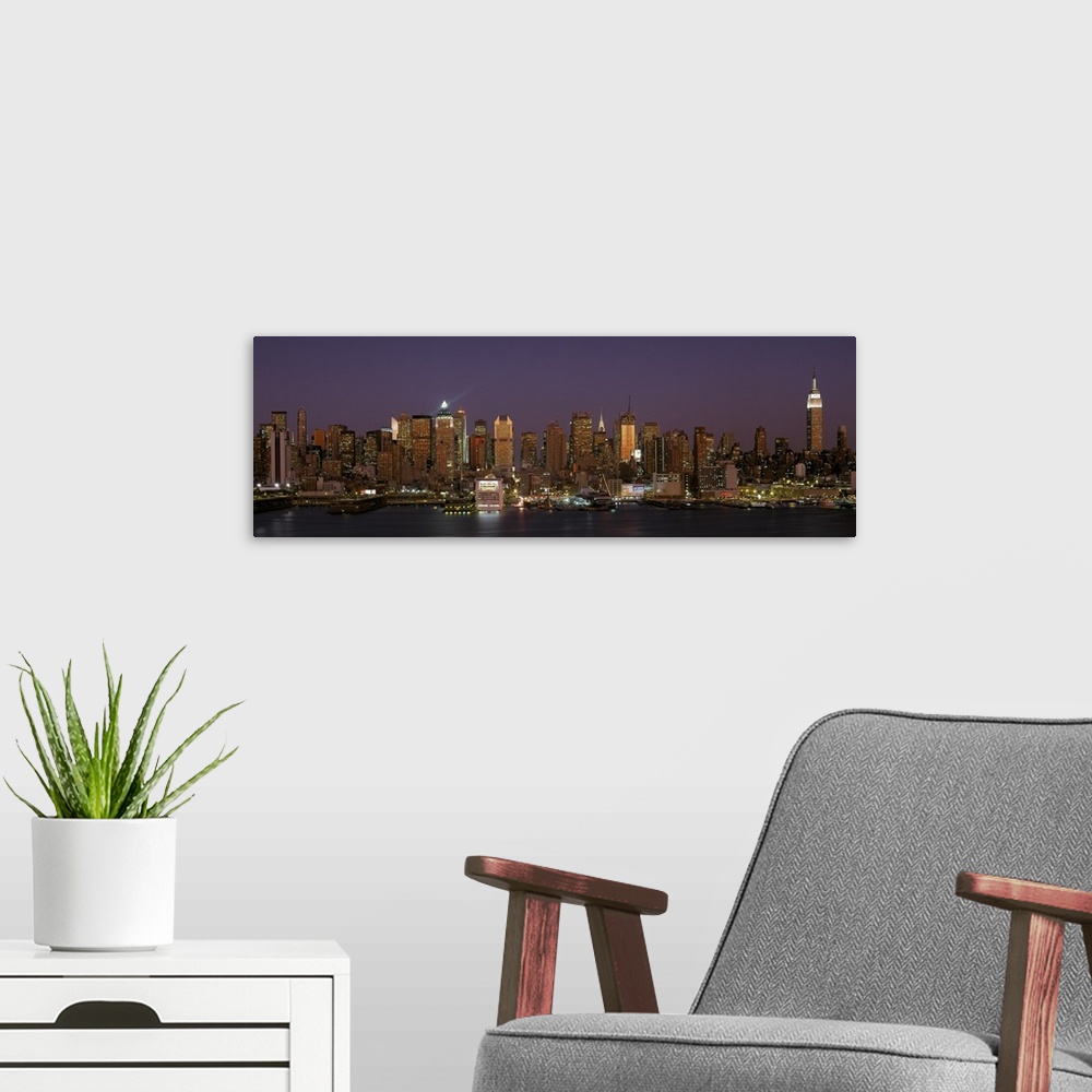 A modern room featuring Wide angel, distant photograph of the Manhattan skyline, lit at night, beneath a deep purple sky ...