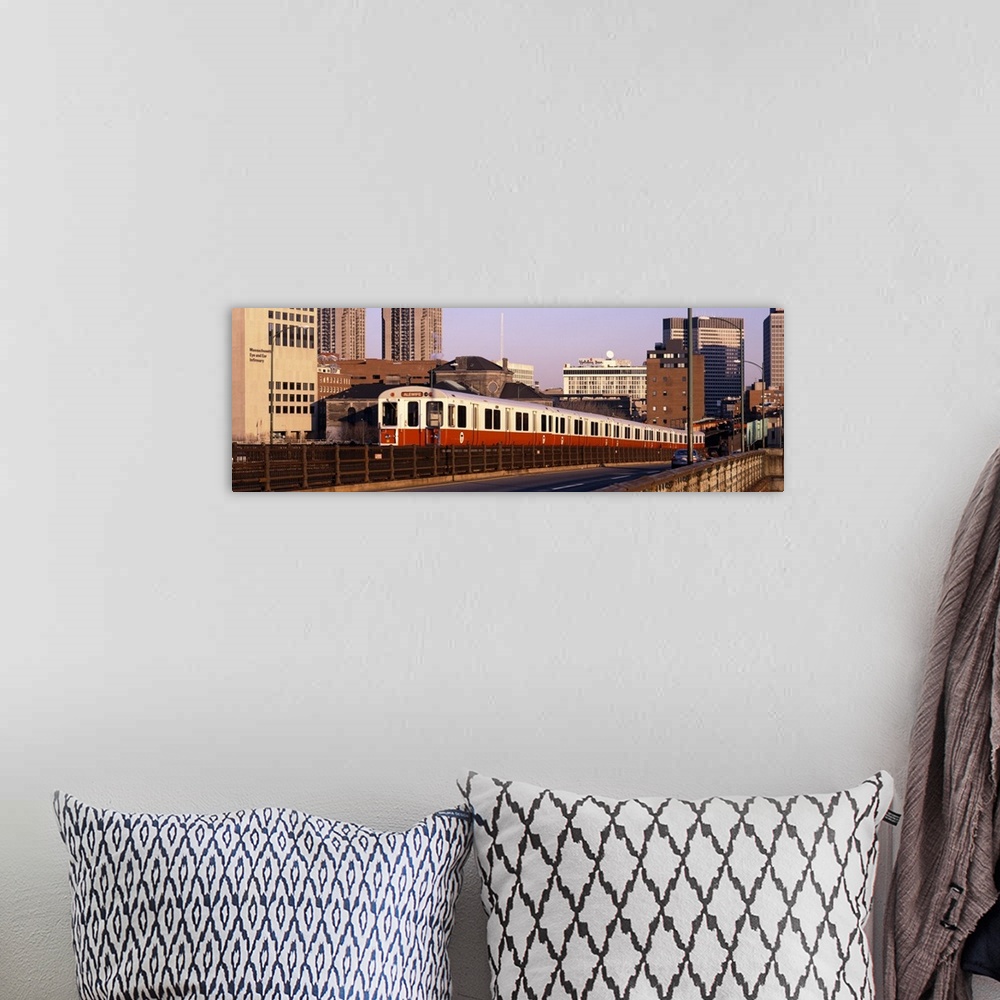 A bohemian room featuring An above ground subway train is photographed in panoramic view with the Boston skyline shown in t...
