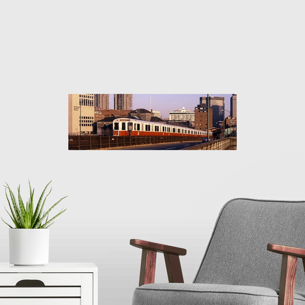 A modern room featuring An above ground subway train is photographed in panoramic view with the Boston skyline shown in t...
