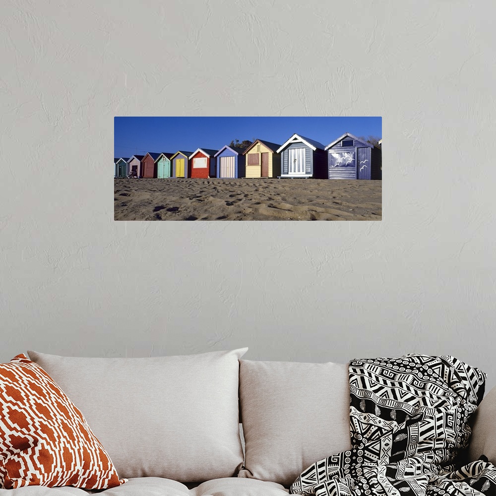 A bohemian room featuring A row of colorful huts are photographed lining the sandy beach.