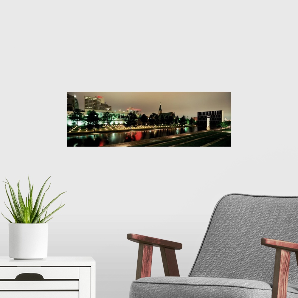 A modern room featuring Panoramic photograph of skyline and waterfront at nigh.  The building lights are reflected in the...
