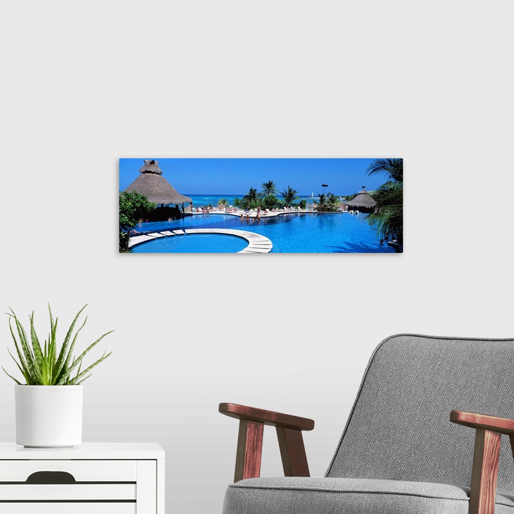 A modern room featuring Panoramic photo print of a big pool with people swimming in it with the ocean in the background.