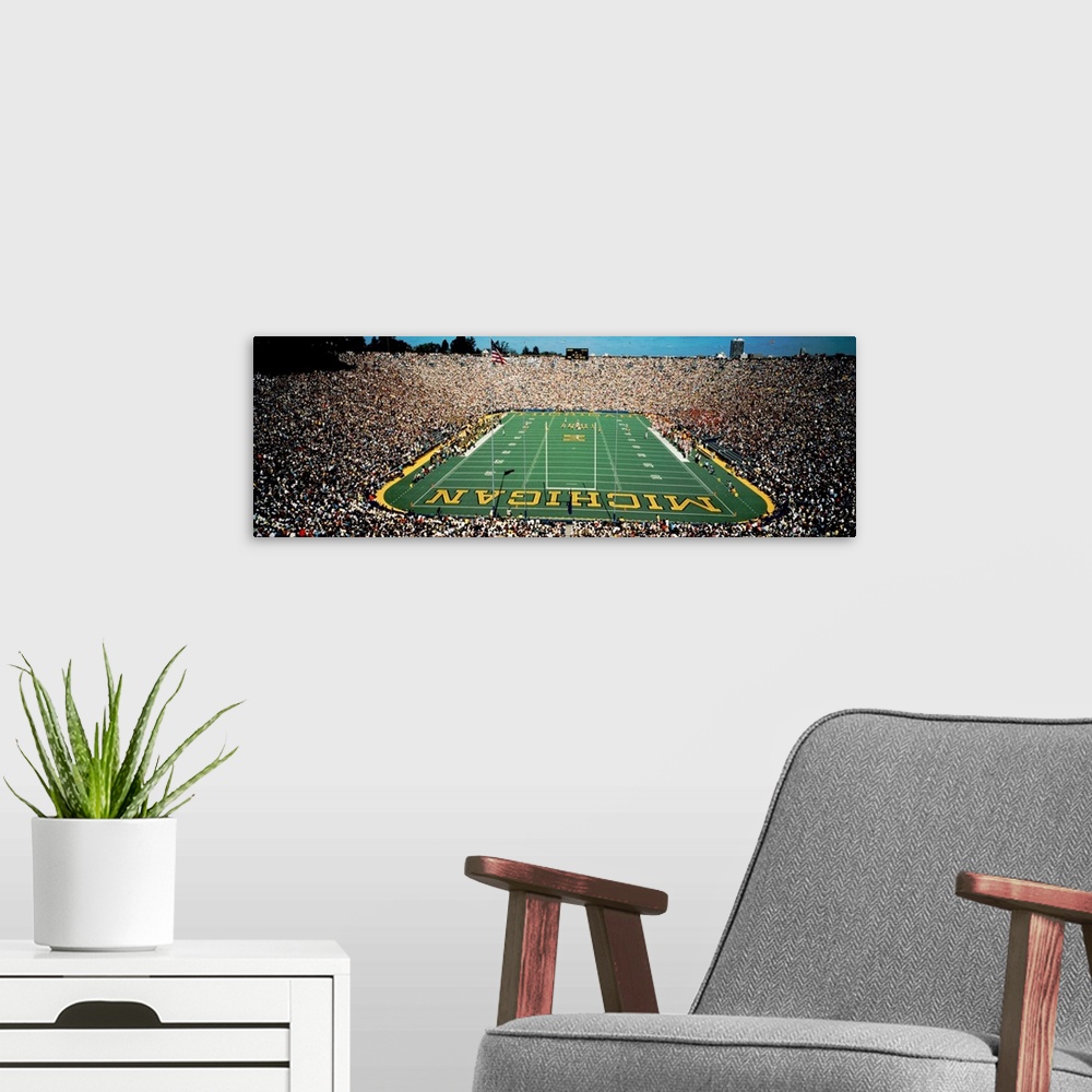 A modern room featuring Panoramic photograph of a college football stadium from behind a the goal.