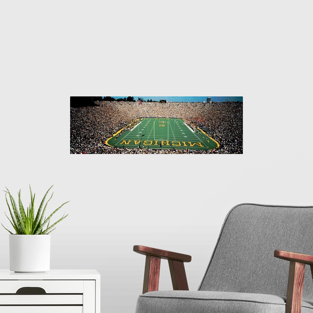 A modern room featuring Panoramic photograph of a college football stadium from behind a the goal.