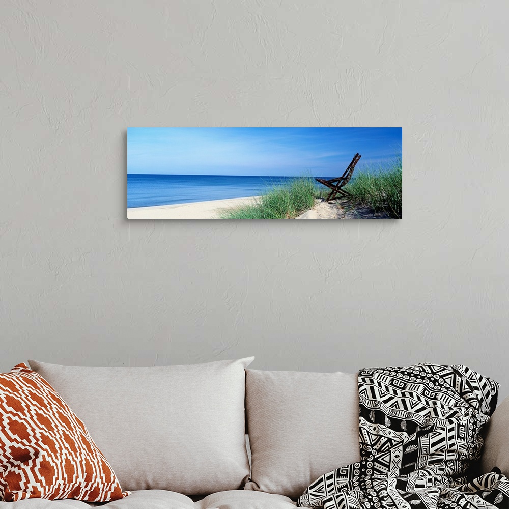 A bohemian room featuring This wall art is a panoramic landscape photograph of a sandy beach with a chair in the dunes over...