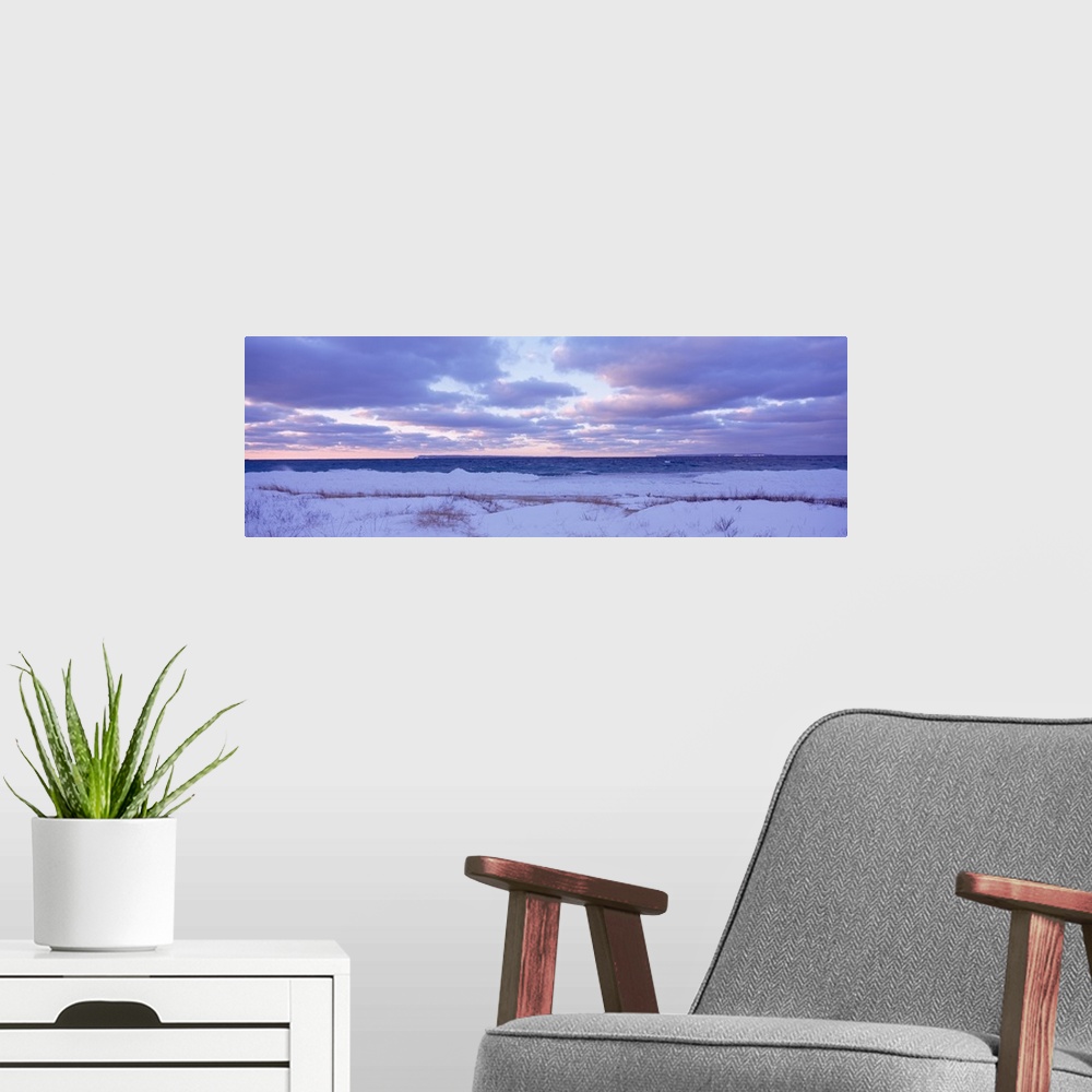 A modern room featuring Large, wide angle photograph of a beach off of Lake Michigan, under a sky of pastels and clouds a...