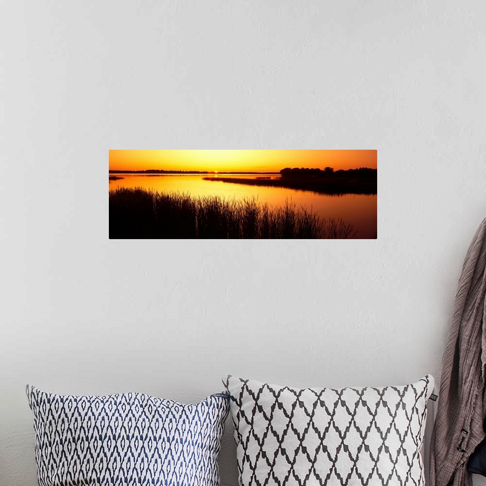 A bohemian room featuring Panoramic image of the last bit of sun peeking at the horizon as it sets behind the reed lined La...