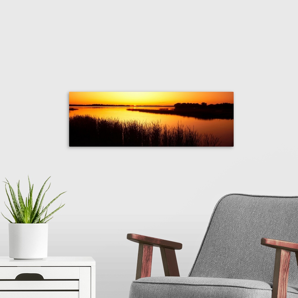 A modern room featuring Panoramic image of the last bit of sun peeking at the horizon as it sets behind the reed lined La...