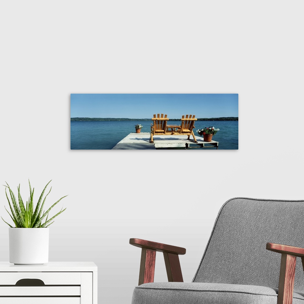 A modern room featuring This panoramic photograph is taken from behind two chairs sitting on a dock looking out over a bo...