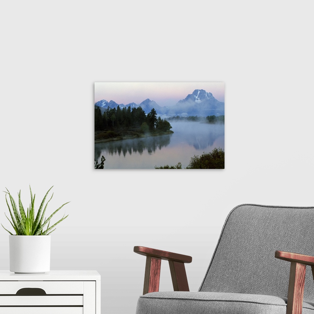 A modern room featuring A large photograph showing forest and foilage surrounding water with mountains in the background ...