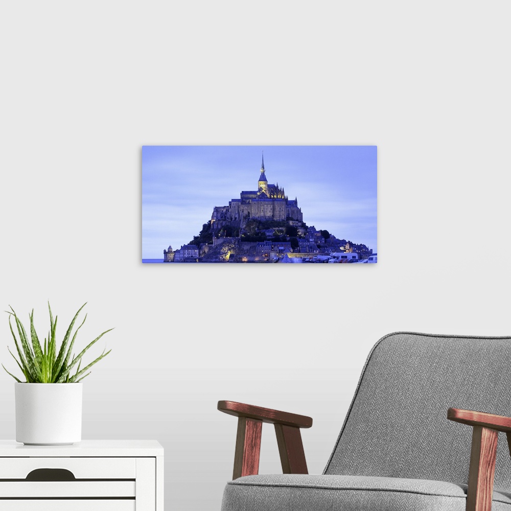 A modern room featuring Dusk shot of a lit up castle sitting high on a small rocky island in the water.