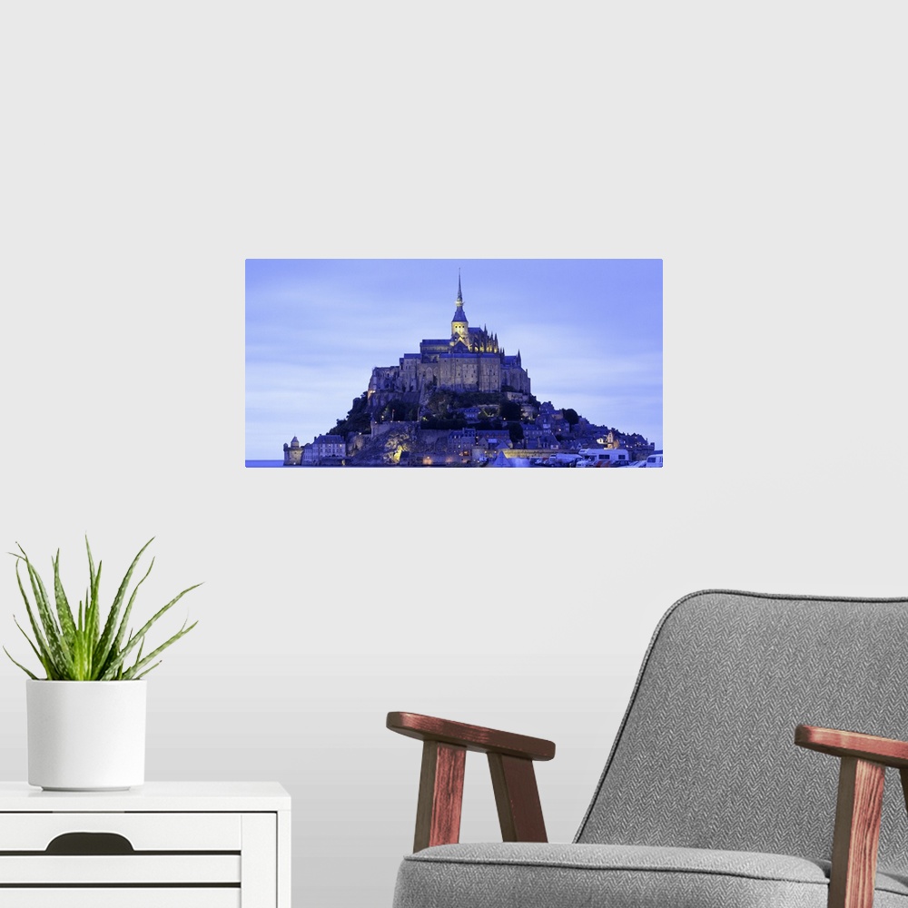 A modern room featuring Dusk shot of a lit up castle sitting high on a small rocky island in the water.