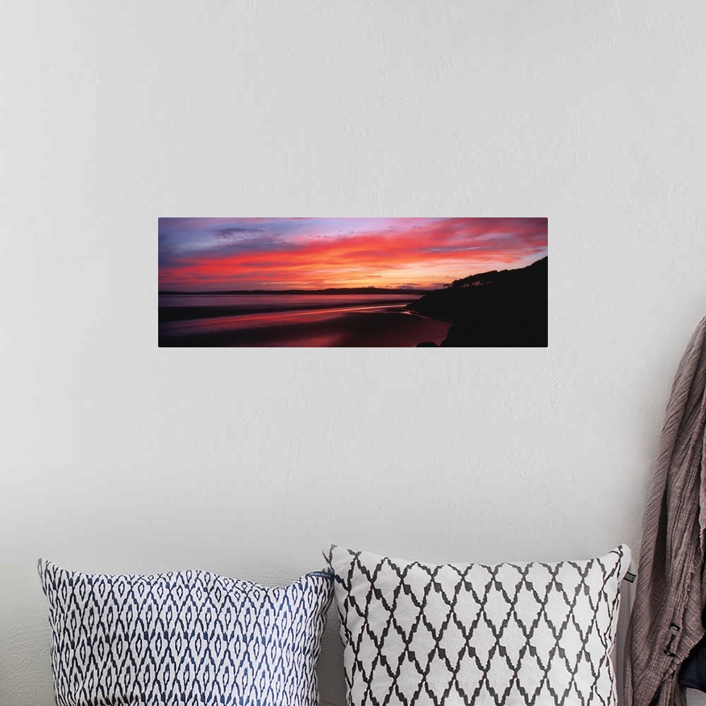 A bohemian room featuring A large panoramic photograph taken of a sunset over a bay in the UK. A hill top is silhouetted to...
