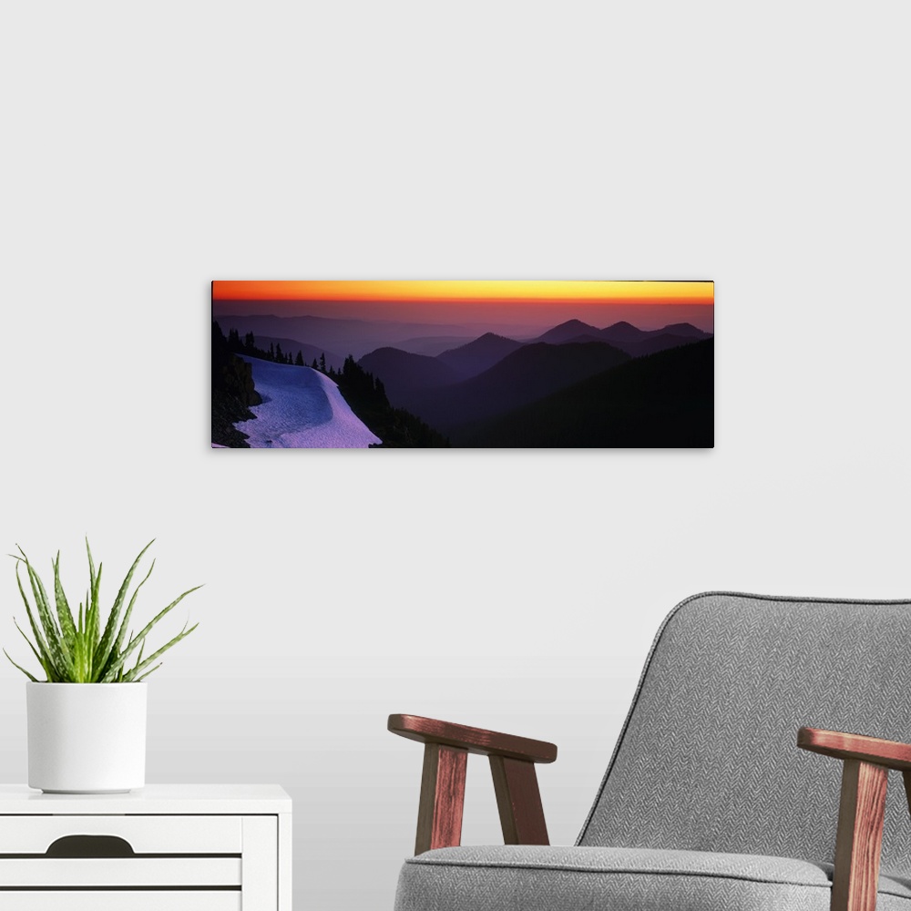 A modern room featuring Mountains in Mount Rainier are silhouetted by the sunset in the background and captured in panora...