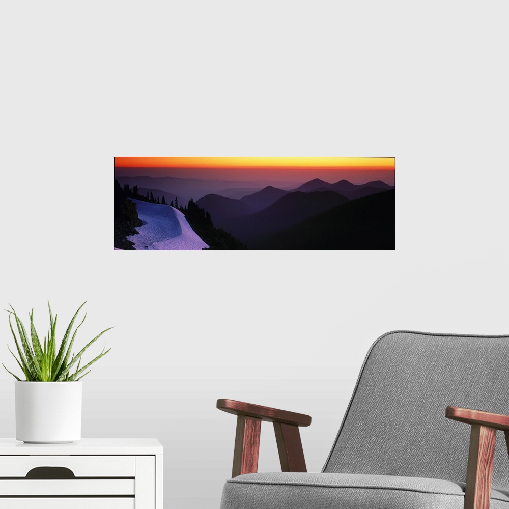 A modern room featuring Mountains in Mount Rainier are silhouetted by the sunset in the background and captured in panora...