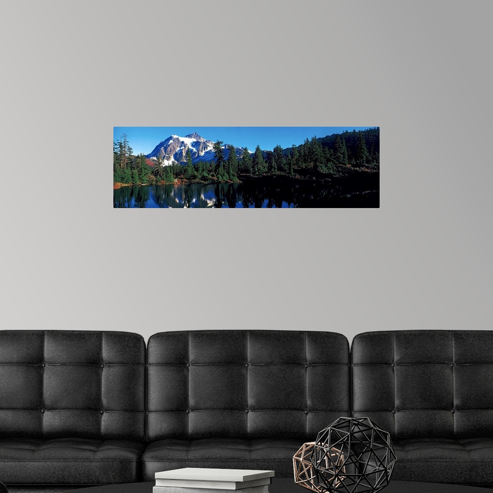 A modern room featuring A snow covered mountain is photographed in panoramic view and just behind a line of pine trees th...