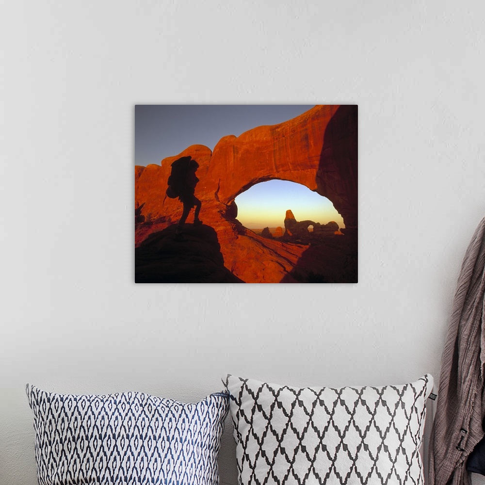 A bohemian room featuring A hiker is photographed looking out onto massive cliffs and arches in a Utah national park.