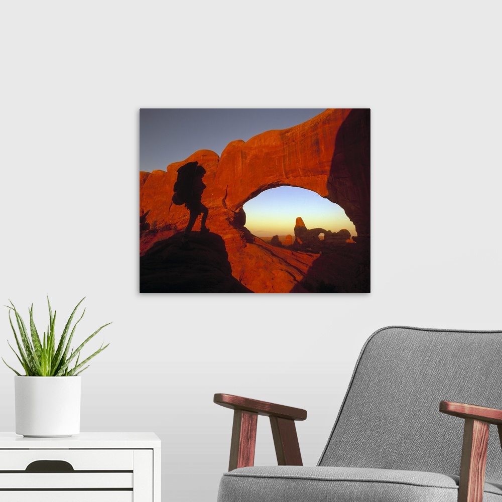A modern room featuring A hiker is photographed looking out onto massive cliffs and arches in a Utah national park.