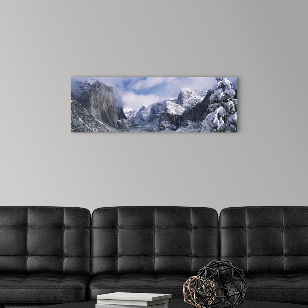 A modern room featuring This panoramic photograph is taken of immense mountains that reach up into the clouds and are cov...
