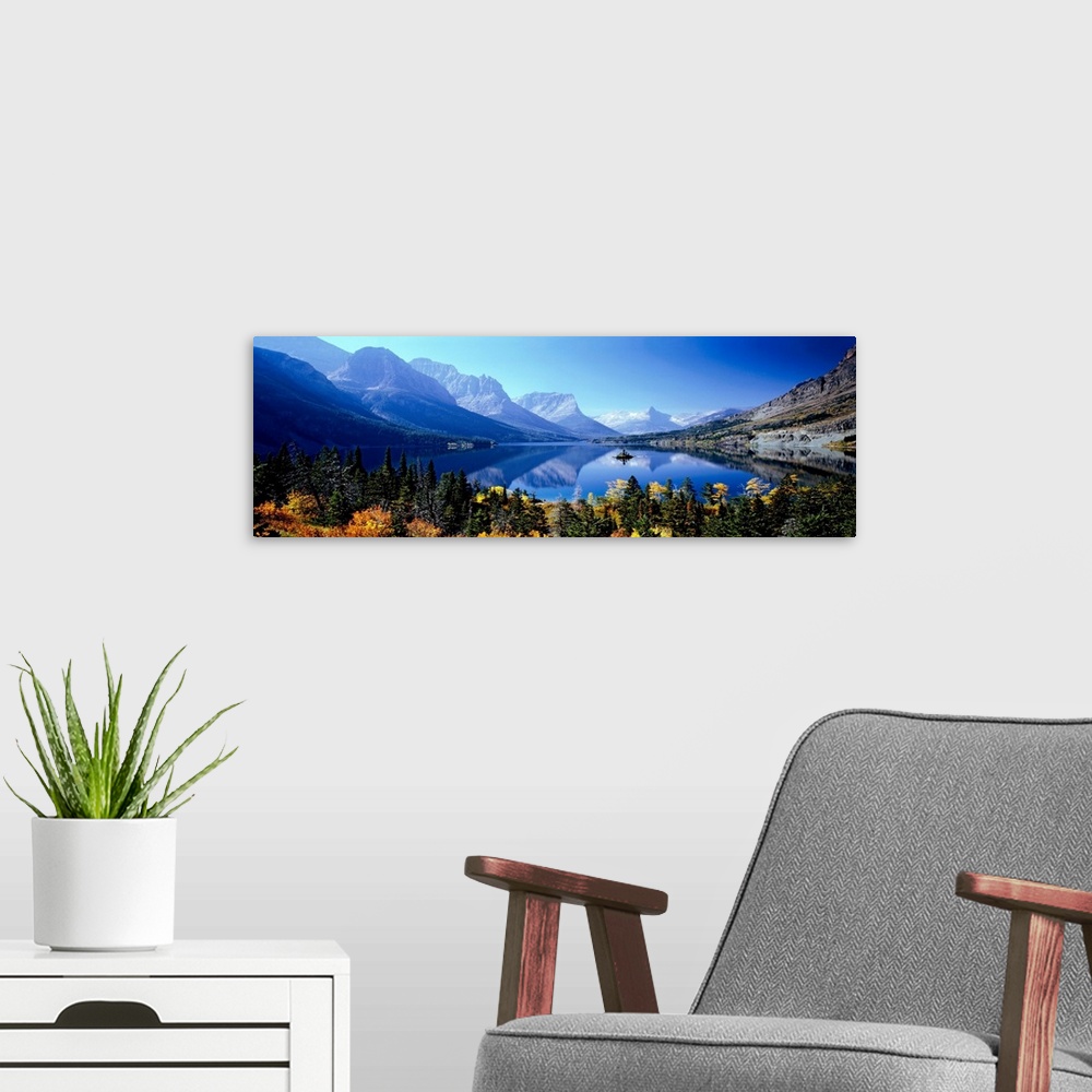 A modern room featuring A panoramic photograph of mountains reflecting in a still lake surrounded by trees in this landsc...
