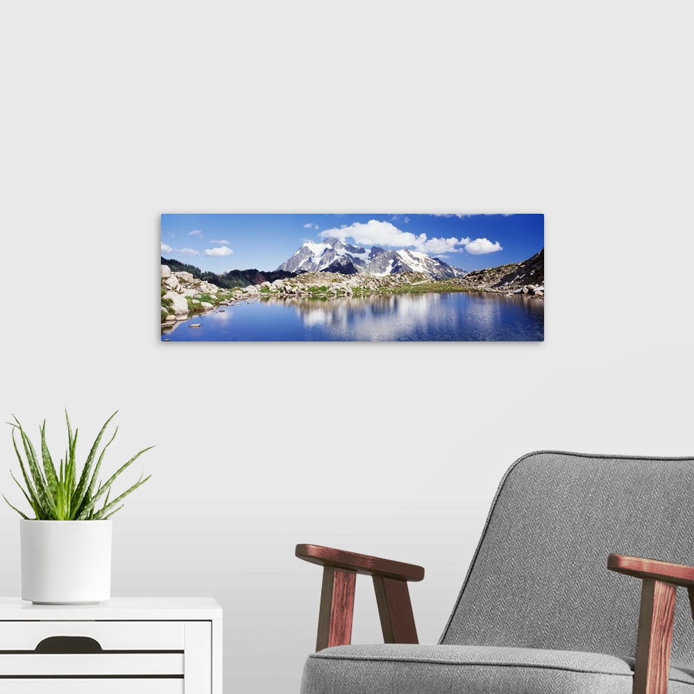 A modern room featuring An immense snow covered mountain is pictured in the background from across a large body of water ...